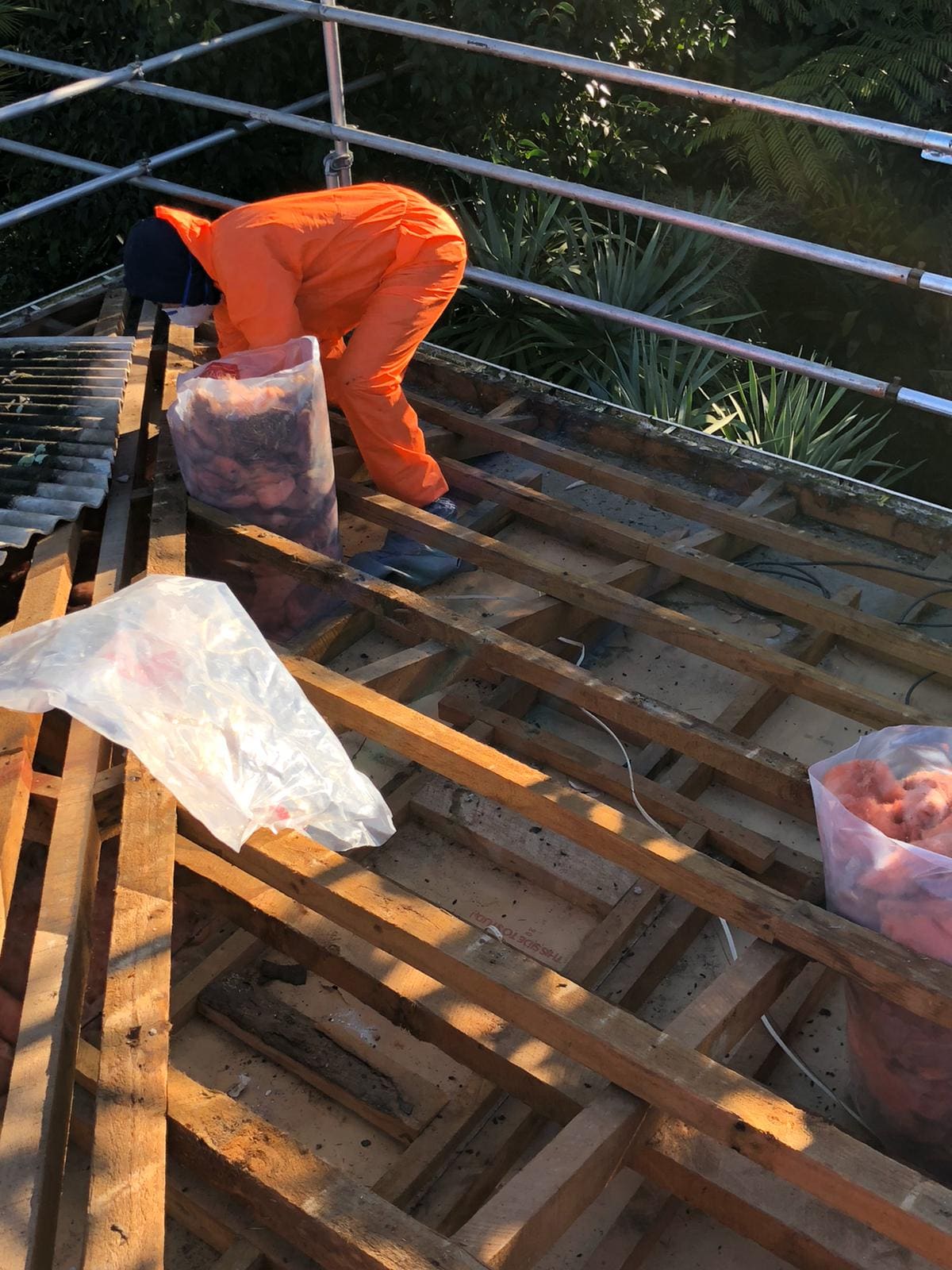 Asbestos removal worker in protective gear wrapping debris on a stripped residential roof